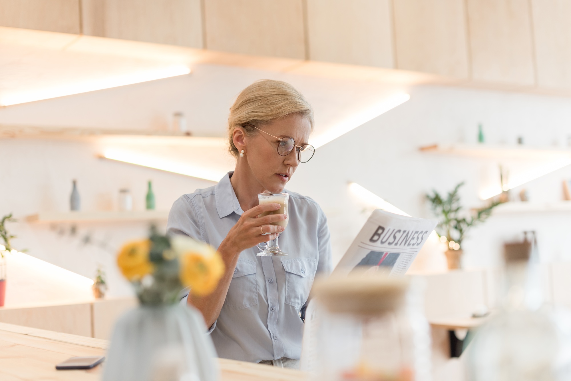 mature businesswoman in eyeglasses reading newspaper and drinking coffee in cafe